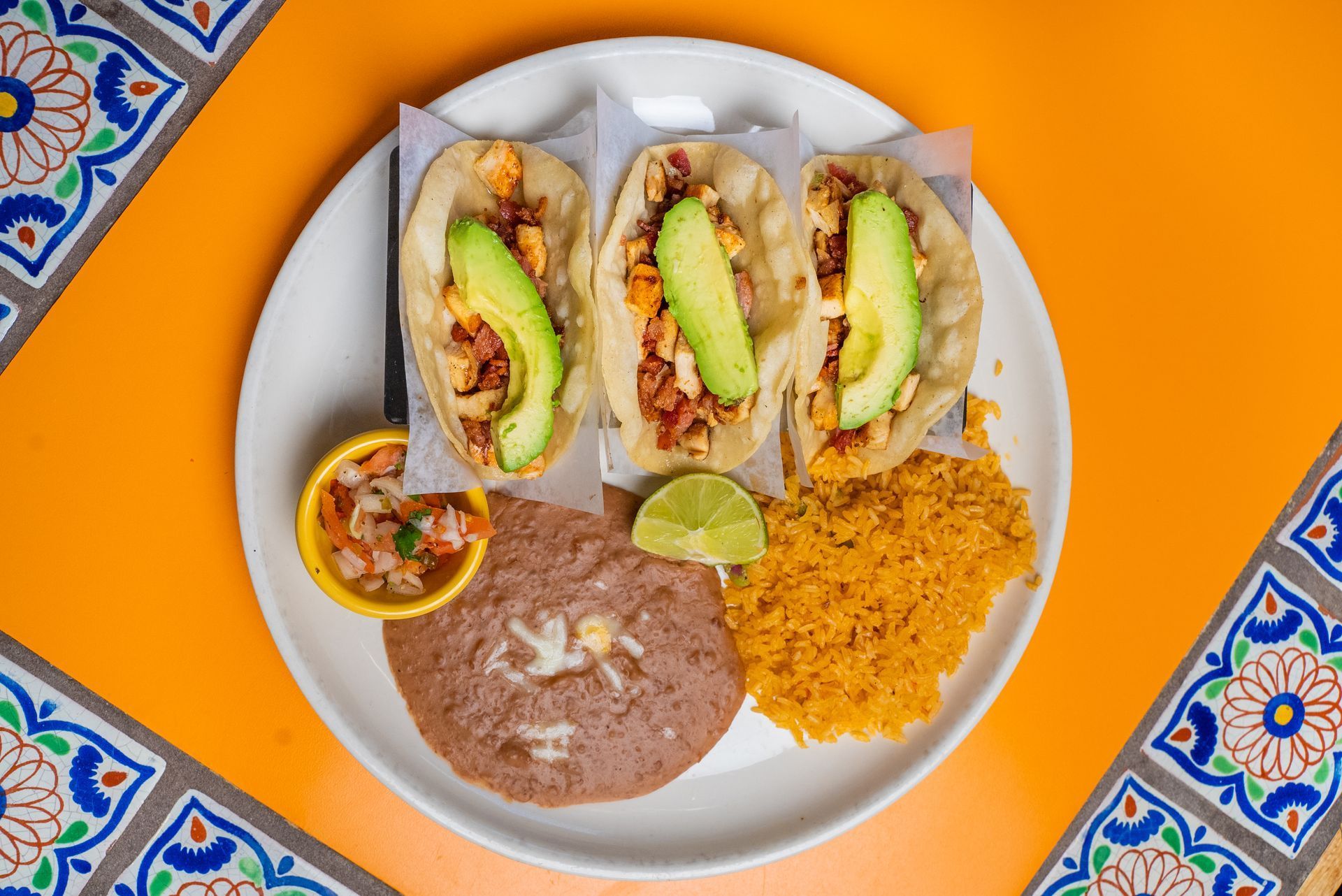 A white plate topped with tacos, avocado, beans, and rice on a table.