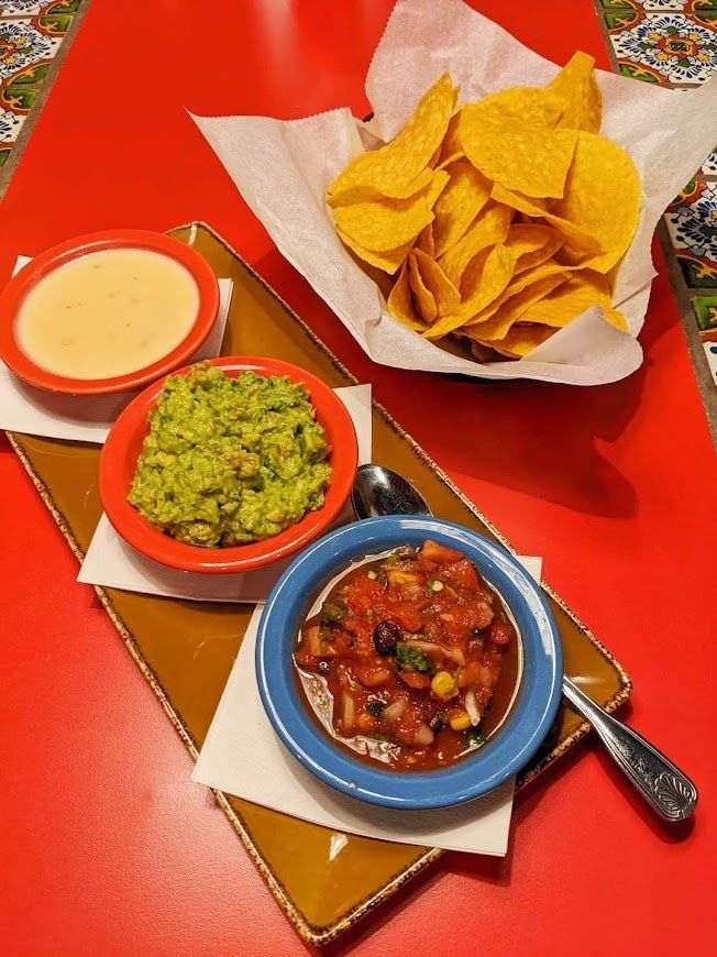 A bowl of guacamole and salsa next to a bowl of tortilla chips.