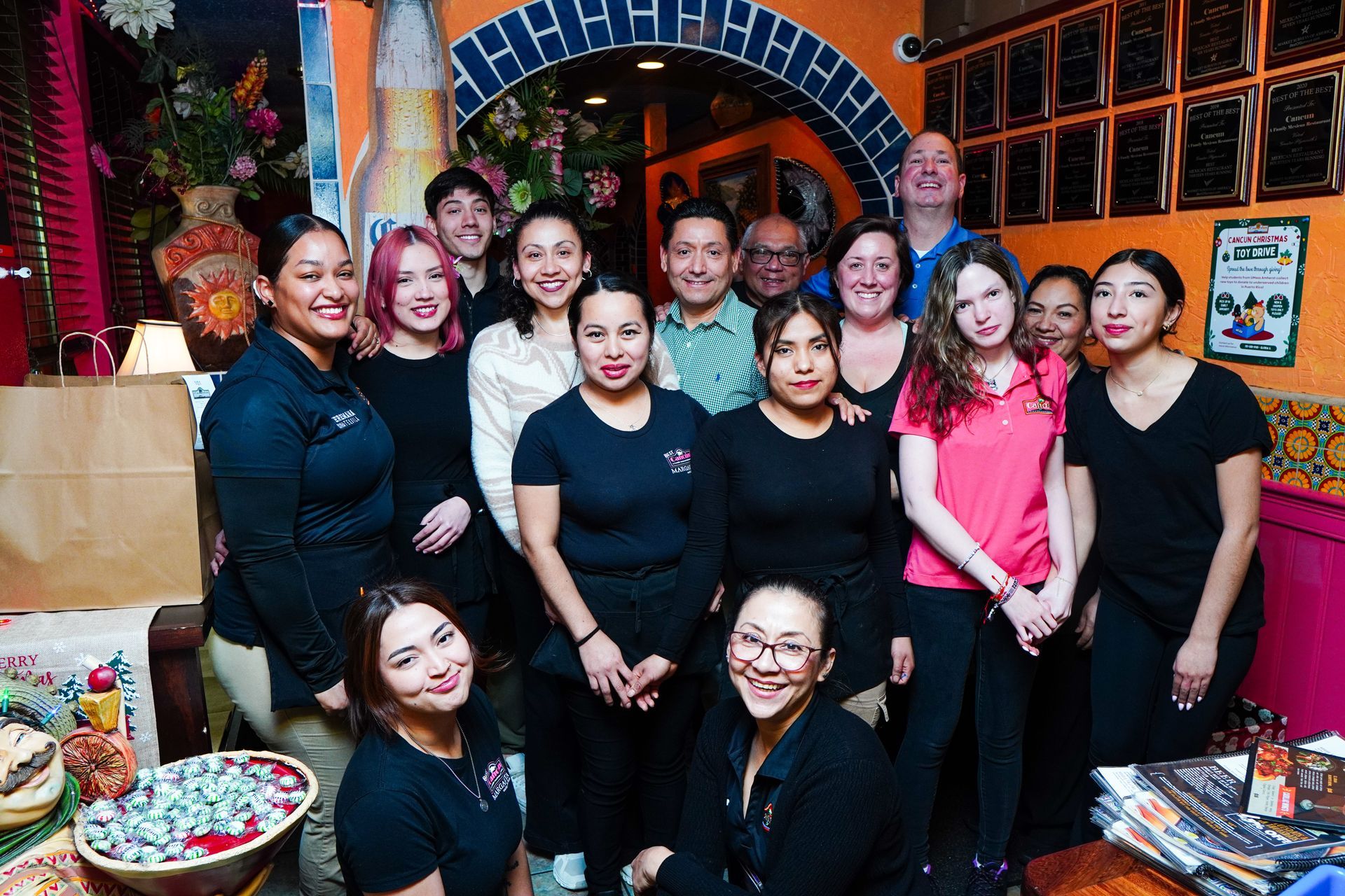 Group of people posing indoors at a festive event, with colorful decorations and an arched backdrop.