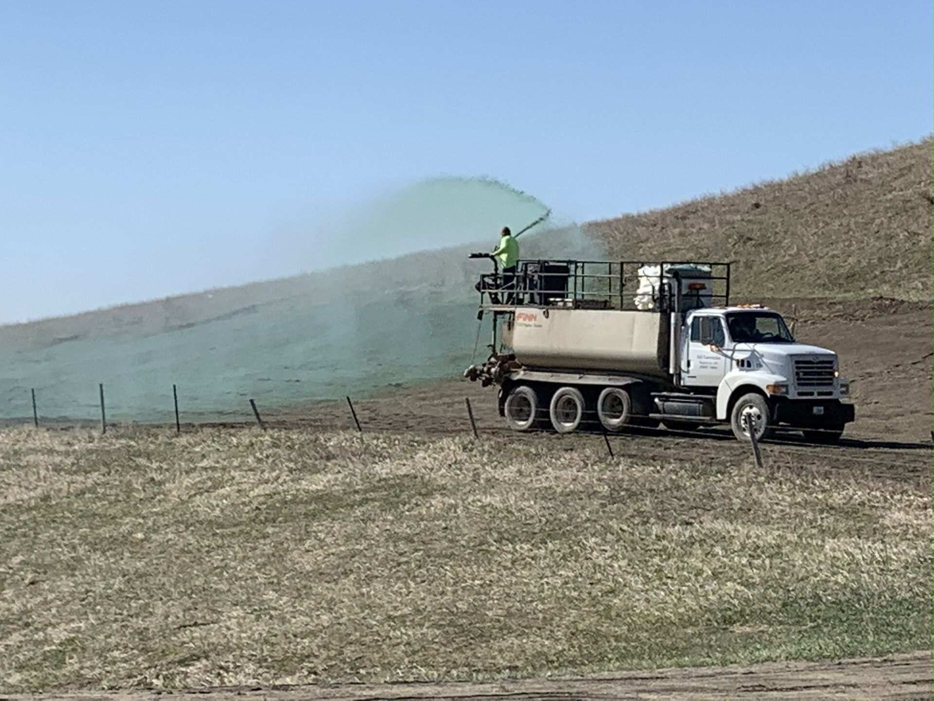 A truck spraying green liquid on a hillside for erosion control.