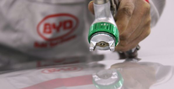 Person holding a paint sprayer, spraying a white surface. The sprayer has green details.