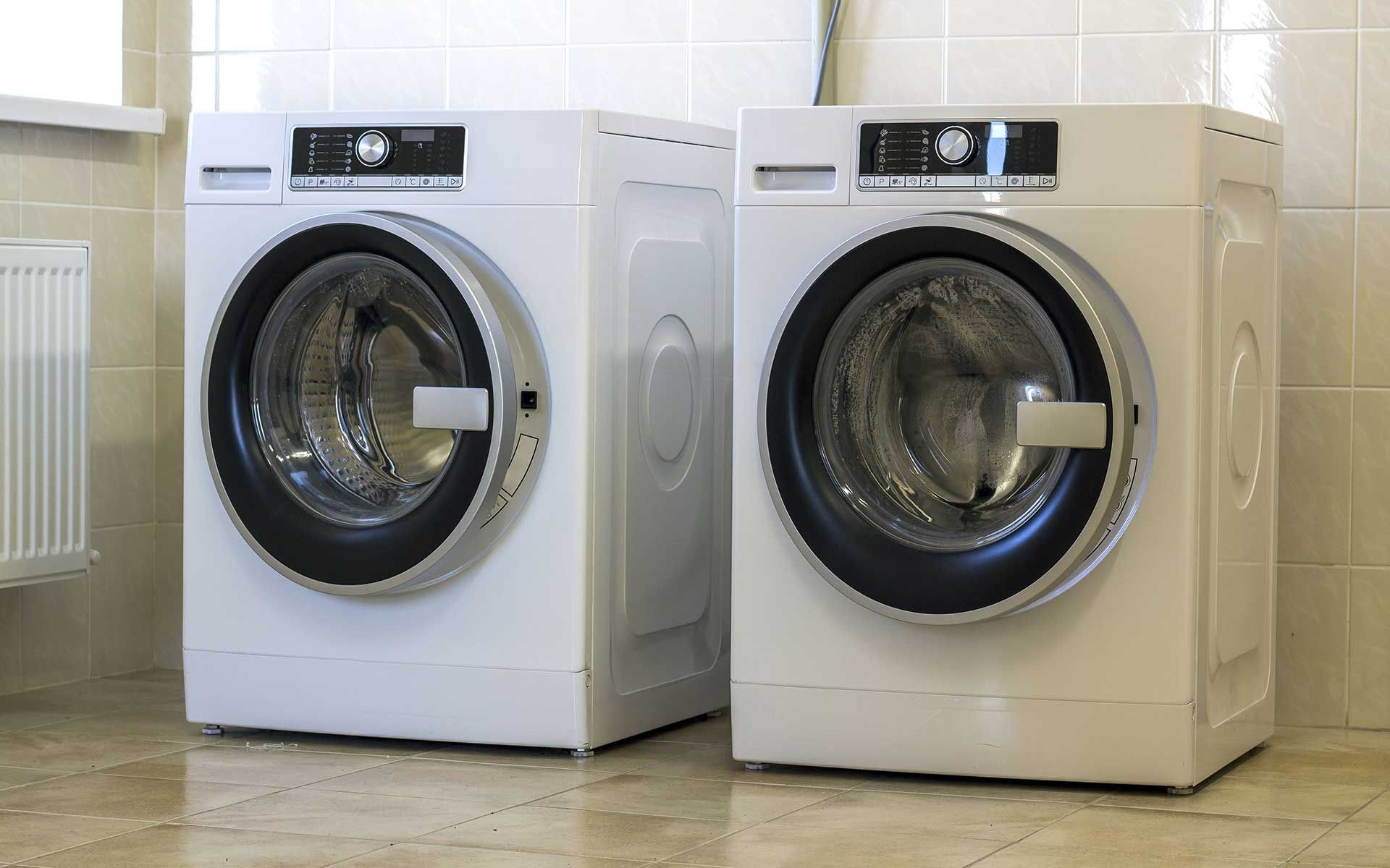 Two white washing machines are sitting next to each other in a laundry room.