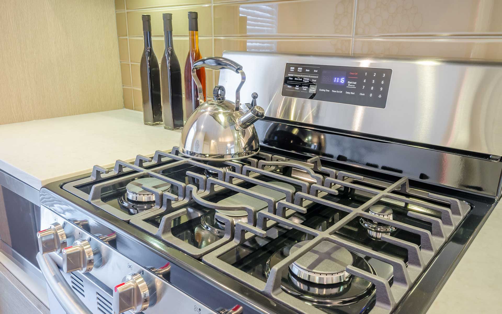 A stainless steel gas stove with a tea kettle on top of it.