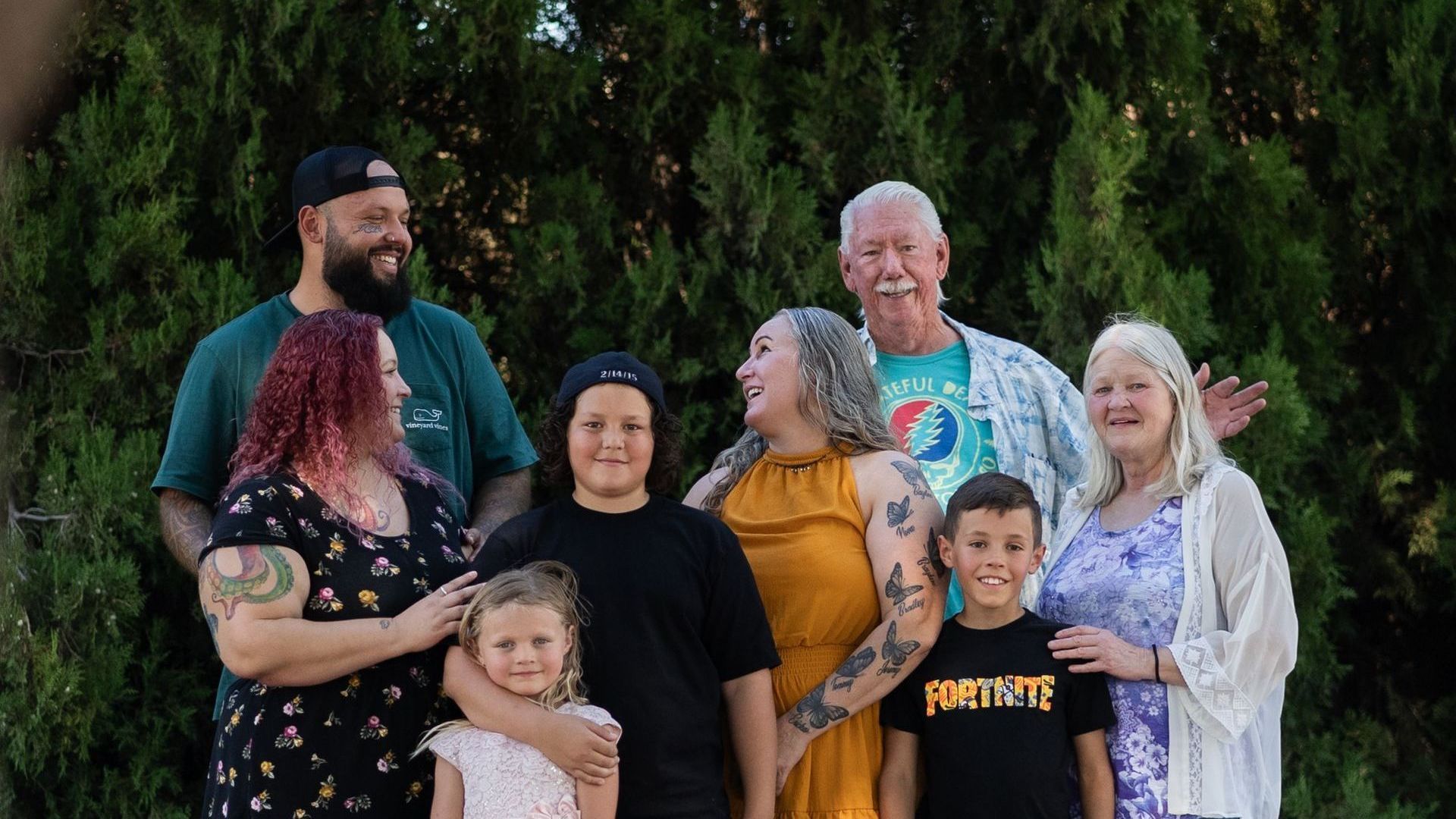 A large family is posing for a picture together in front of trees.