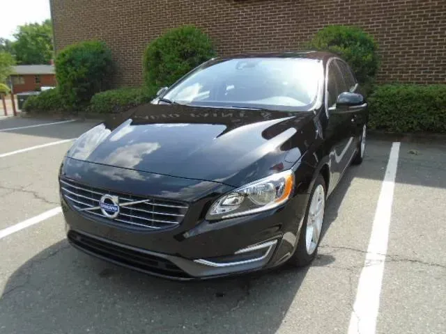 Black Volvo sedan parked in a lot beside a brick building and bushes