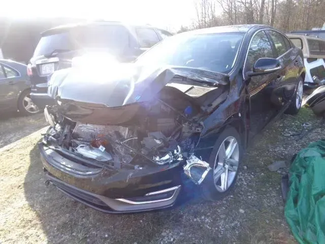 Damaged black sedan with severe front-end collision damage in a parking lot, sun glare on windshield