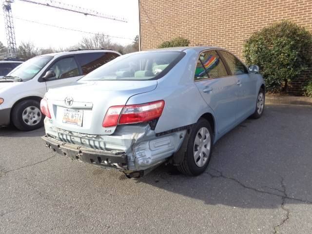 Damaged silver sedan with rear bumper torn off, parked in a lot beside another car