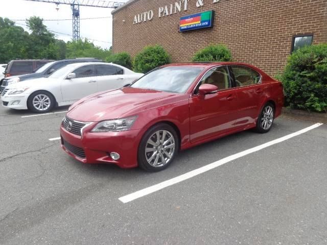 Red sedan parked in front of an auto paint shop, with a white car beside it.
