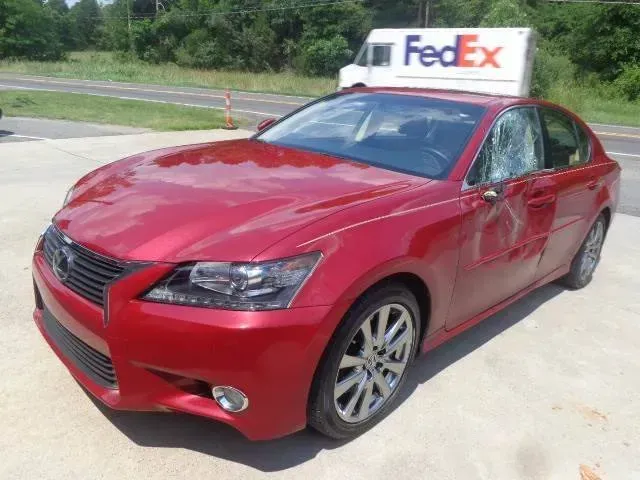 Red sedan with a FedEx sign on top, parked on a concrete lot near grass and trees.