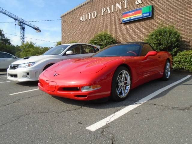 Red sports car parked outside an auto paint shop, with a white car beside it.