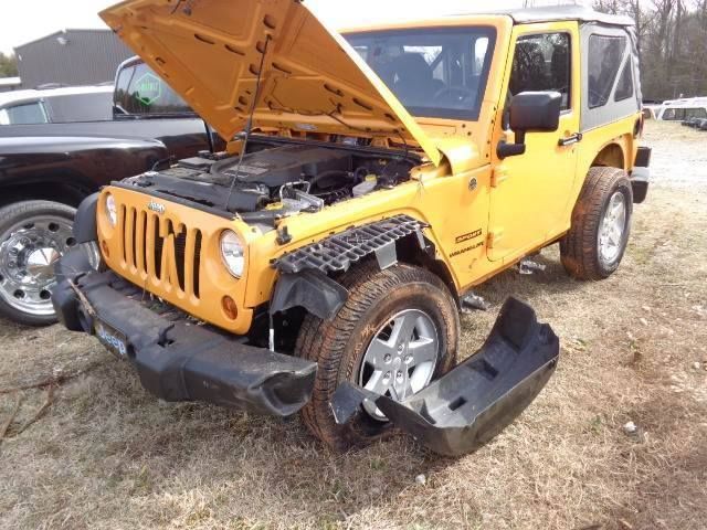Yellow Jeep with front-end damage, hood open, and detached bumper in a grassy lot