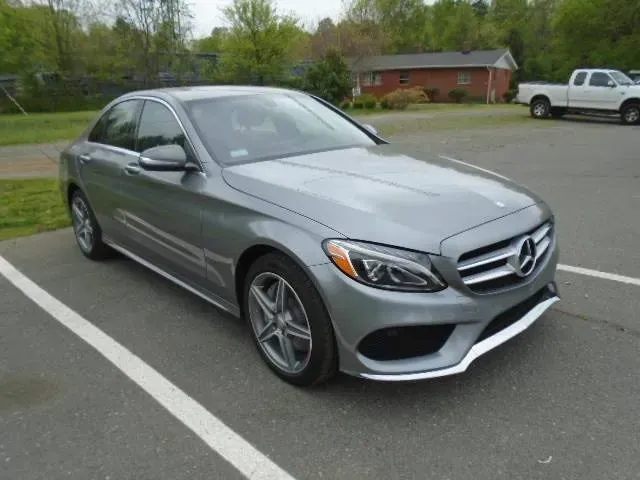 Silver Mercedes-Benz sedan parked on a paved lot with trees and a house in the background
