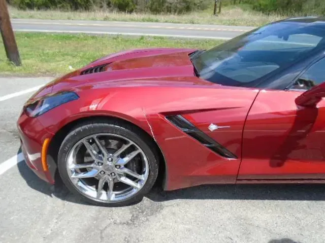 Red sports car parked on a road, showing the front side and wheel.
