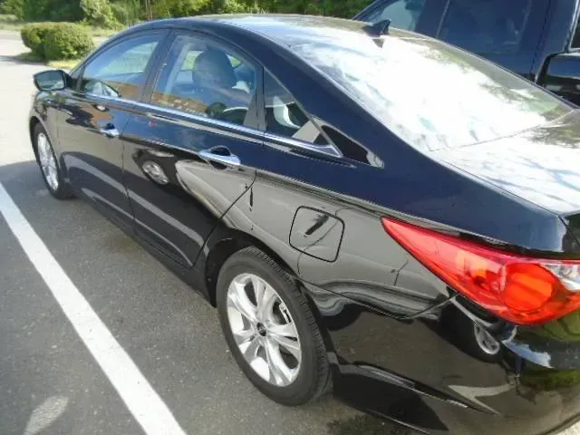 Black sedan parked in a lot, rear side view with silver wheels and red taillight.