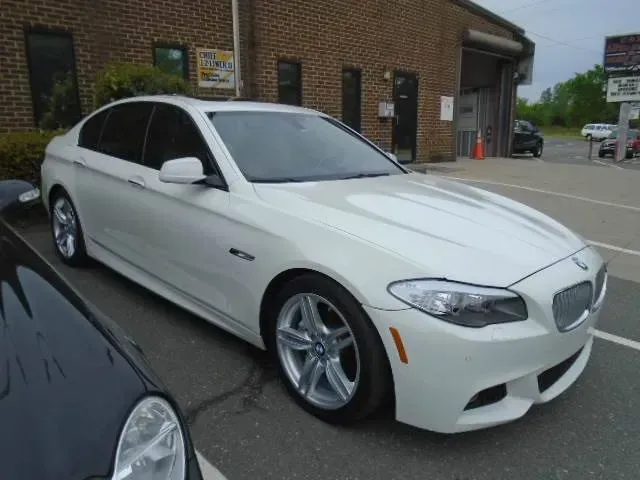 White BMW sedan parked outside a brick building, front-left view, with tinted windows and silver rims