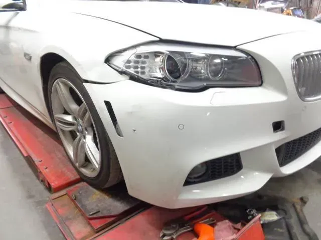 White BMW on a tow truck platform, front bumper damaged and wheel misaligned.