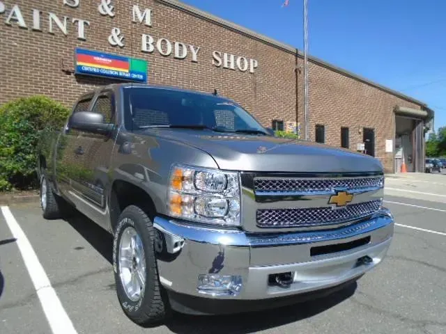 Silver Chevrolet pickup parked outside a paint and body shop building