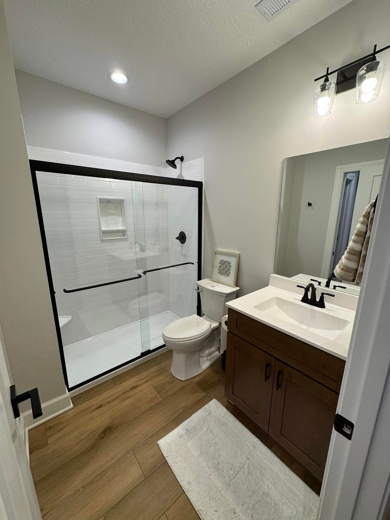 Modern bathroom with a white shower, wood-look floor, and dark brown vanity.