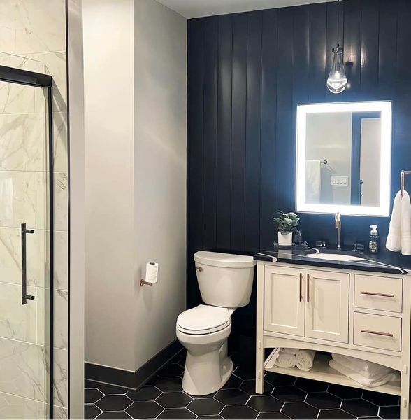 Bathroom with black and white accents. Dark blue accent wall, white vanity, black hexagon floor tiles, and a glass shower.