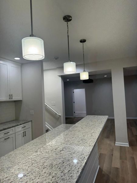Kitchen with a granite countertop island and three pendant lights. White cabinets and light wood floors.