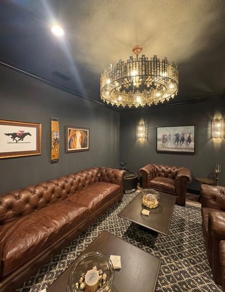 Leather sofa and armchairs in a dark room with horse art, a patterned rug, and a large chandelier.