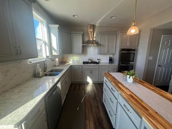 A modern kitchen with gray cabinets, granite countertops, and a wooden island.