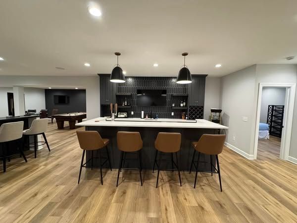 Modern basement bar with brown stools, black pendant lights, and wood-look flooring.