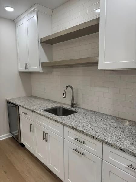 White kitchen cabinets with granite countertop, sink, and open shelving.