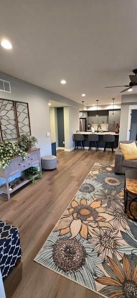 Living room with sunflower rug, wooden floors, and a view into the kitchen.
