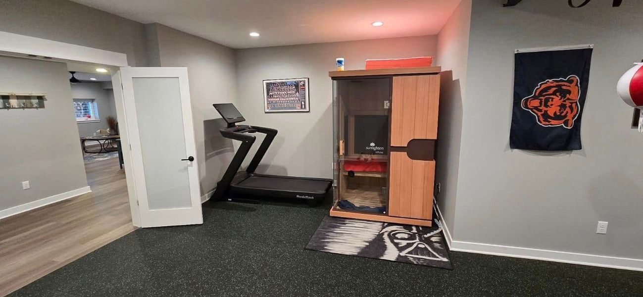 Home gym with treadmill, wooden cabinet, Chicago Bears flag, and punching bag.