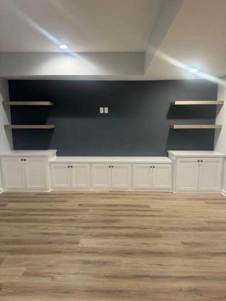 Built-in entertainment center with a dark wall, white cabinets, and wooden shelves above a wooden floor.
