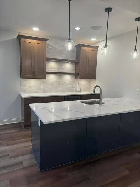 Modern kitchen with dark blue island and wood cabinets, white countertops, and pendant lights.