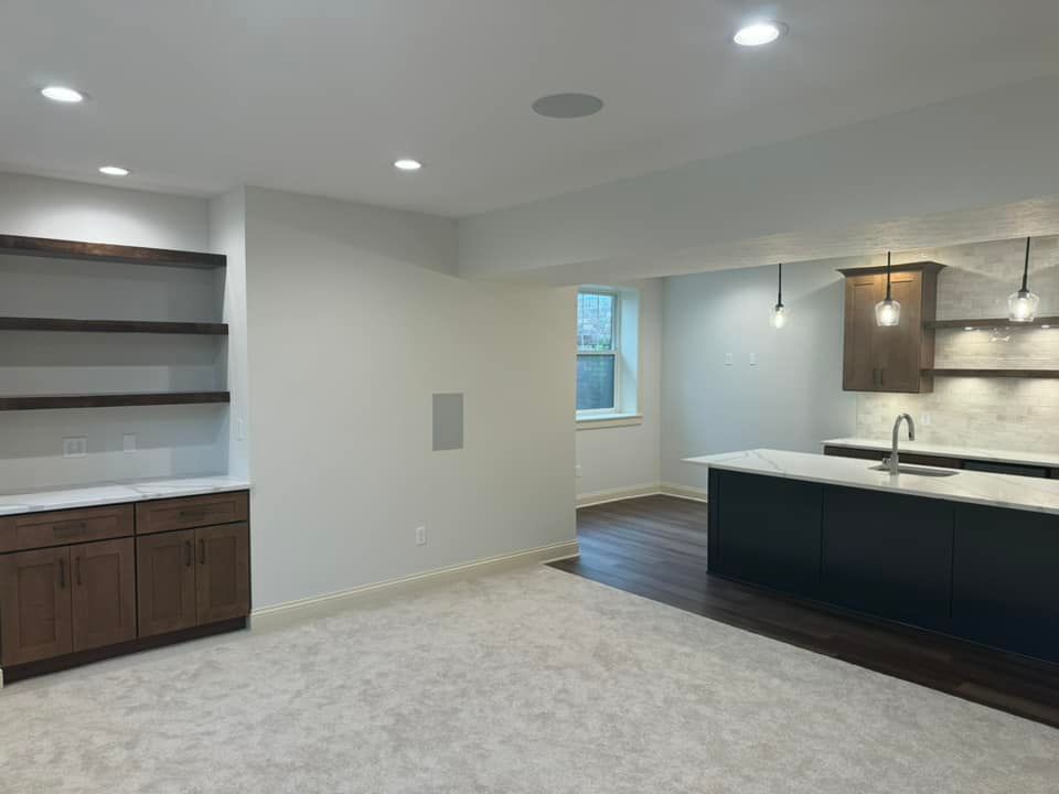 Basement with kitchen. White walls, wood cabinets/shelves, black island, light carpet, recessed lighting.