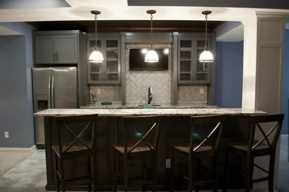Basement bar with grey cabinets, granite countertop, bar stools, and pendant lights.