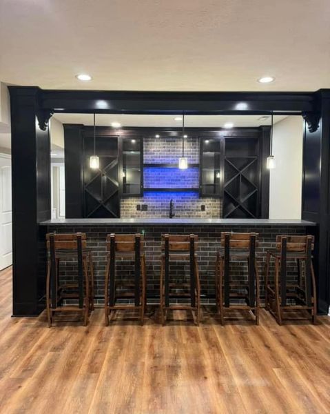 A finished basement bar with black cabinetry, brick backsplash, and wooden stools.