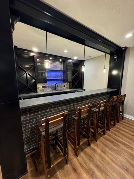 Interior view of a home bar with a brick facade, black cabinets, countertop, and bar stools.