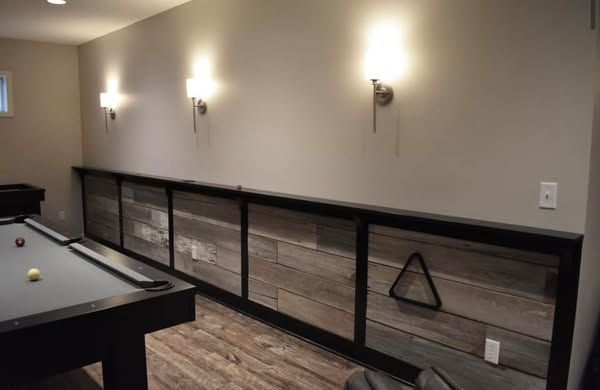 Pool table in a basement. Reclaimed wood paneling along a wall with sconce lighting above.
