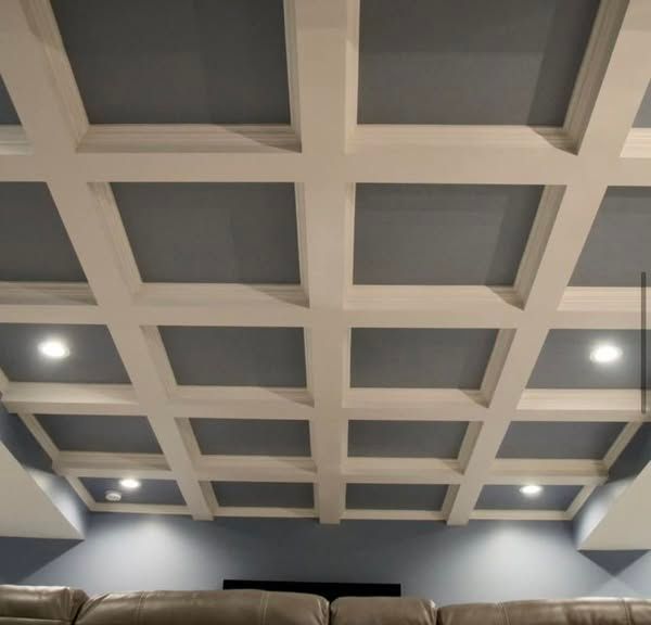 White coffered ceiling with recessed lighting above a gray wall and tan sofa.