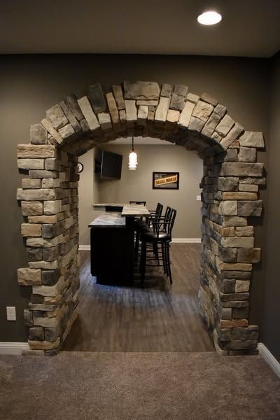 Stone archway leading to a bar area with dark cabinets, stools, and a small TV.