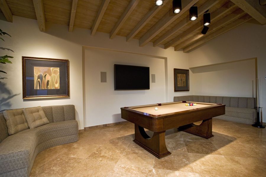 Pool table in a game room with art, a curved sofa, and a wall-mounted TV.