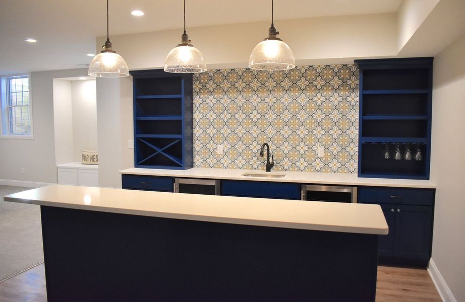 Basement bar with blue cabinets, patterned backsplash, pendant lights, and a white countertop.