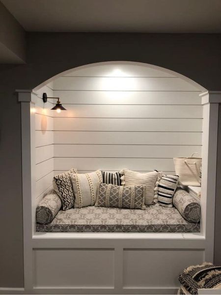 Cozy white built-in reading nook with pillows, cushions, and a small black wall sconce.