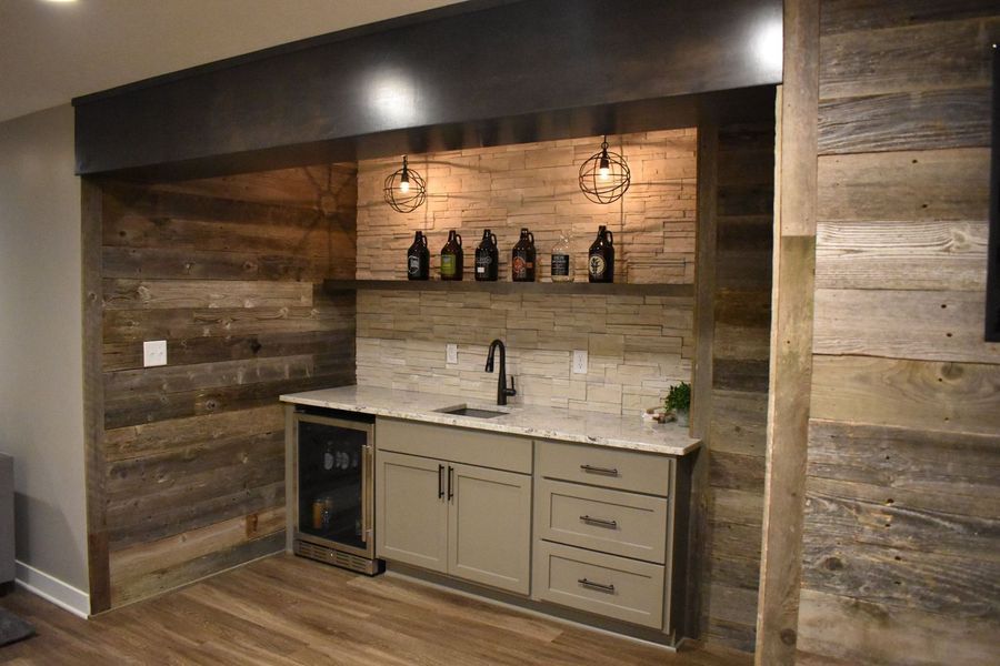 A rustic home bar with wooden walls, cabinets, a sink, and beer bottles on a shelf.