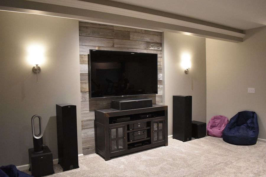 Home theater setup: TV mounted on wood accent wall, flanked by speakers, with entertainment center and sconce lights.
