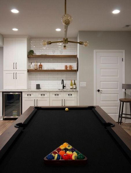 Pool table in a basement bar area with white cabinets, wood shelves, and a door.