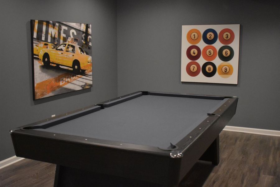 Pool table in a room with two paintings on gray walls.