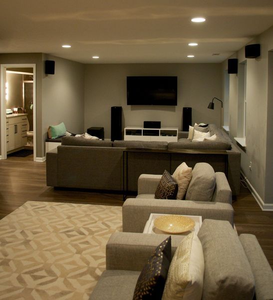 Modern gray living room with sectional sofa, TV, and speakers. Beige patterned rug, recessed lighting.
