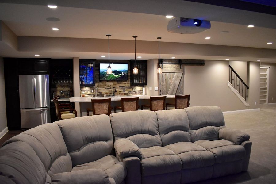 Finished basement with bar, sectional sofa, TV, and projector screen.