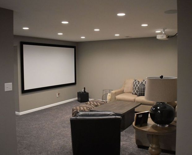 Home theater: large screen on gray wall, beige couch, dark carpet, recessed lights.