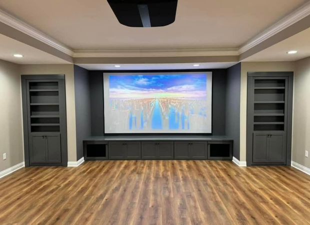 Home theater with screen centered in a gray alcove, flanked by bookshelves and cabinets. Wooden floor.